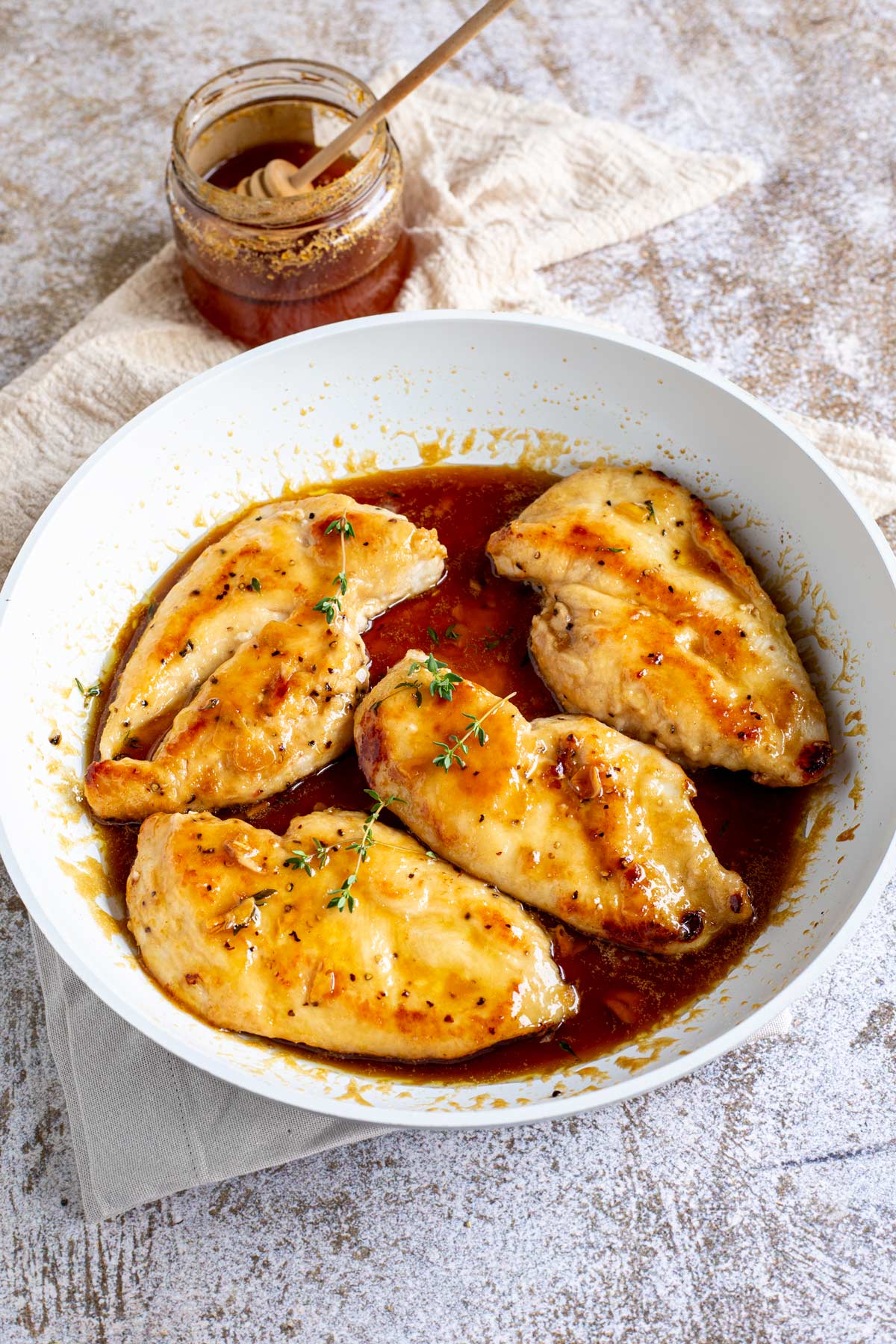 a skillet on a rustic wood table with 4 chicken breasts in a honey sauce