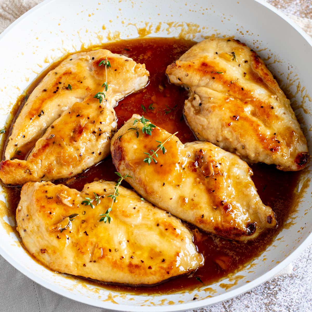 close up of 4 chicken breasts in a skillet with a deep brown sticky sauce