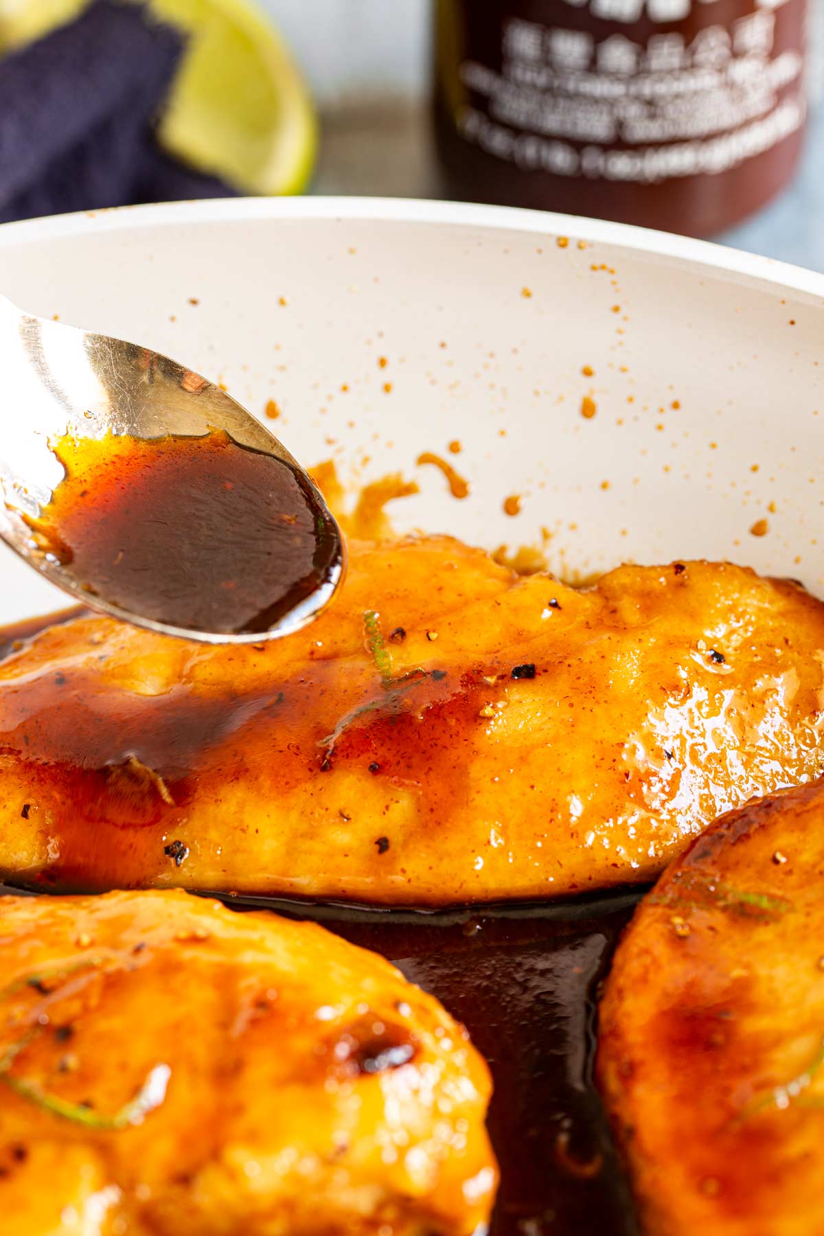 a spoon drizzling a sticky sauce over a cooked chicken breast