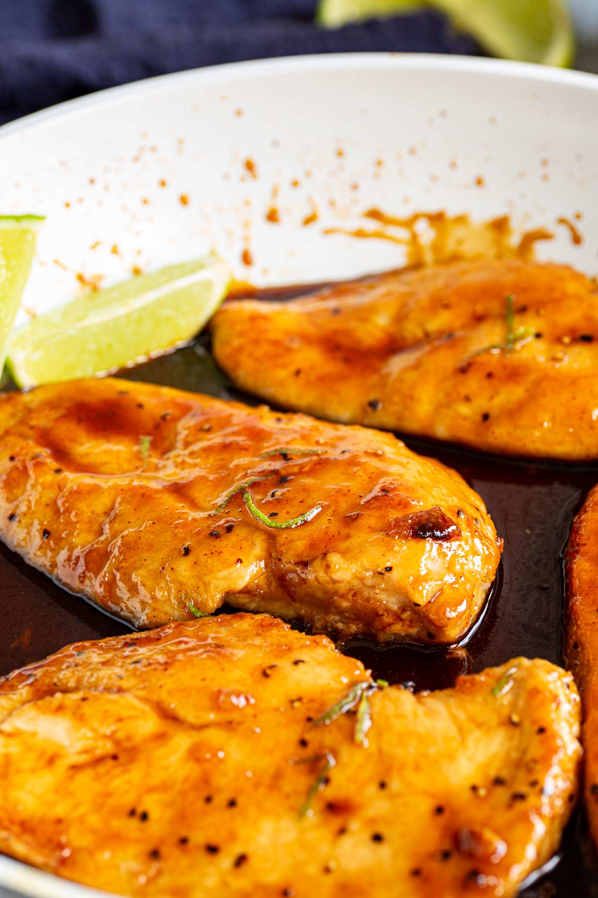 4 chicken breasts in a white skillet with lime wedges and sauce