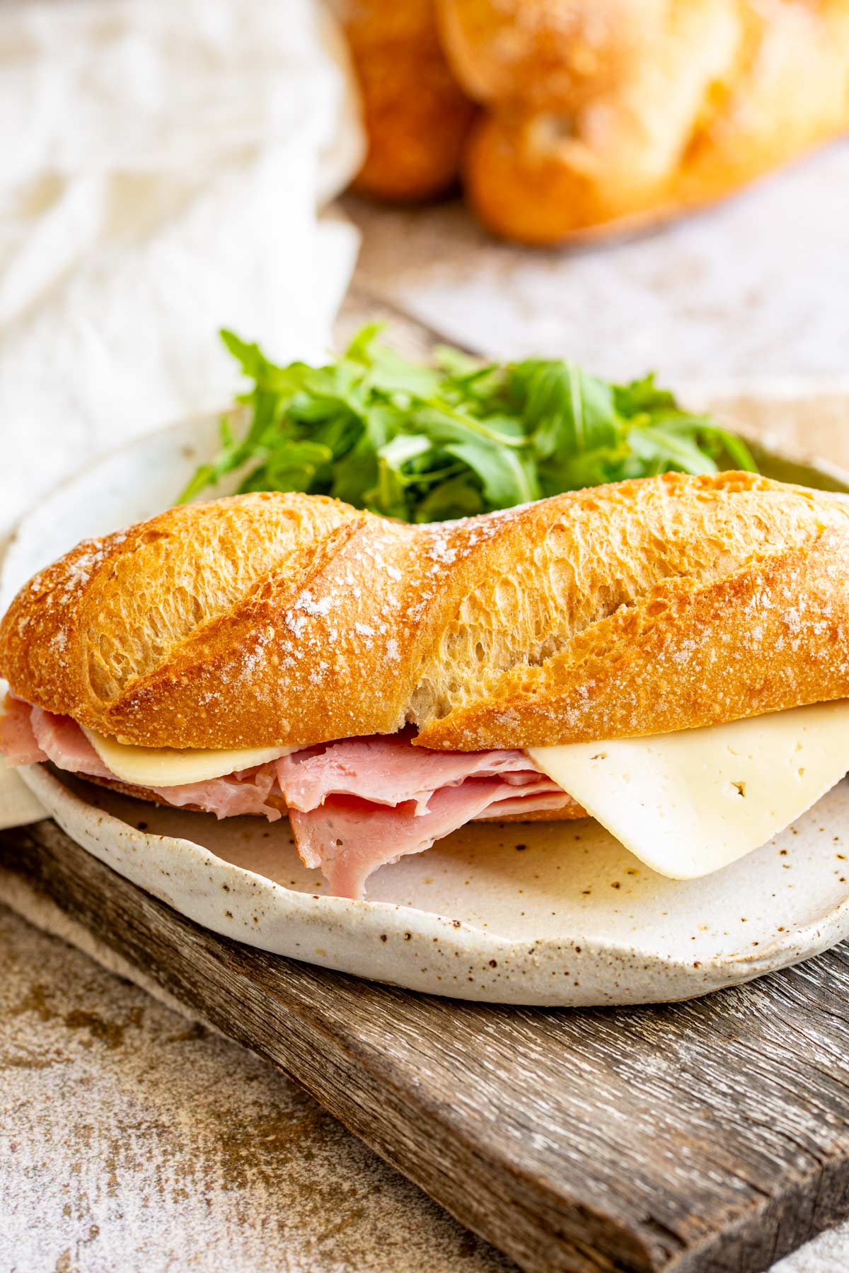 a crusty mini baguette filled with ham and cheese on a rustic plate