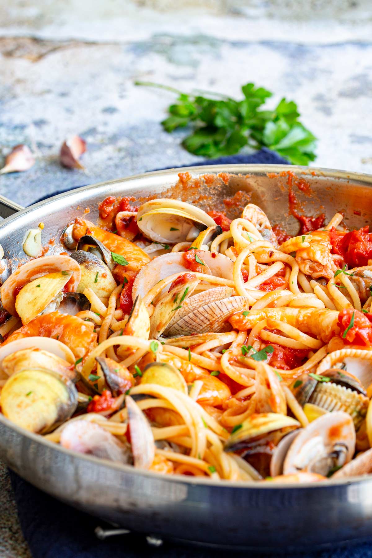 a silver skillet filled with pasta and seafood on a stone table