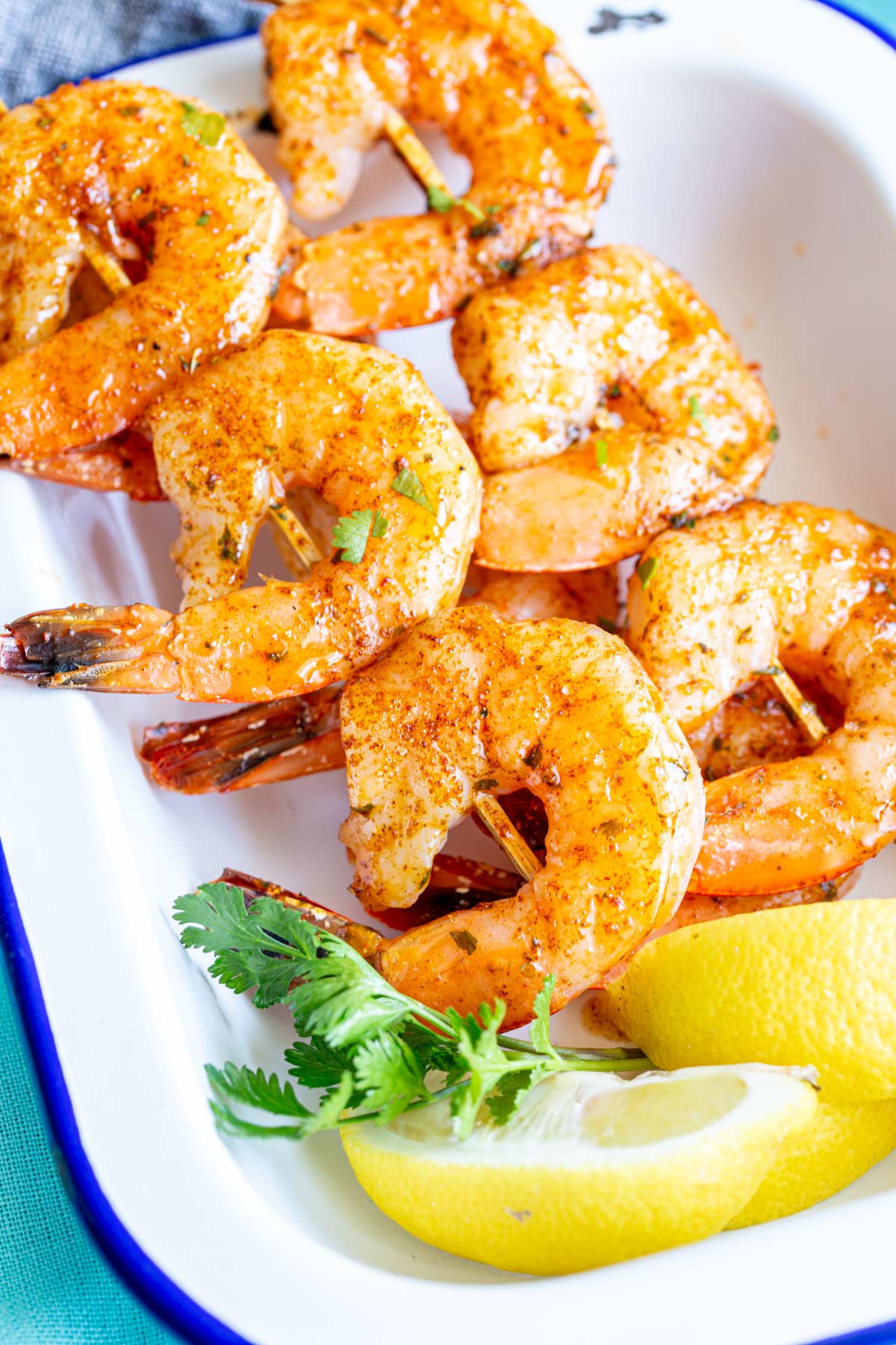 shrimp skewers in a white dish with lemon and coriander garnish