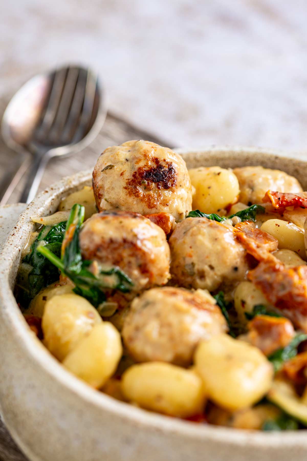 close up on a meatball sat on a bowl of gnocchi