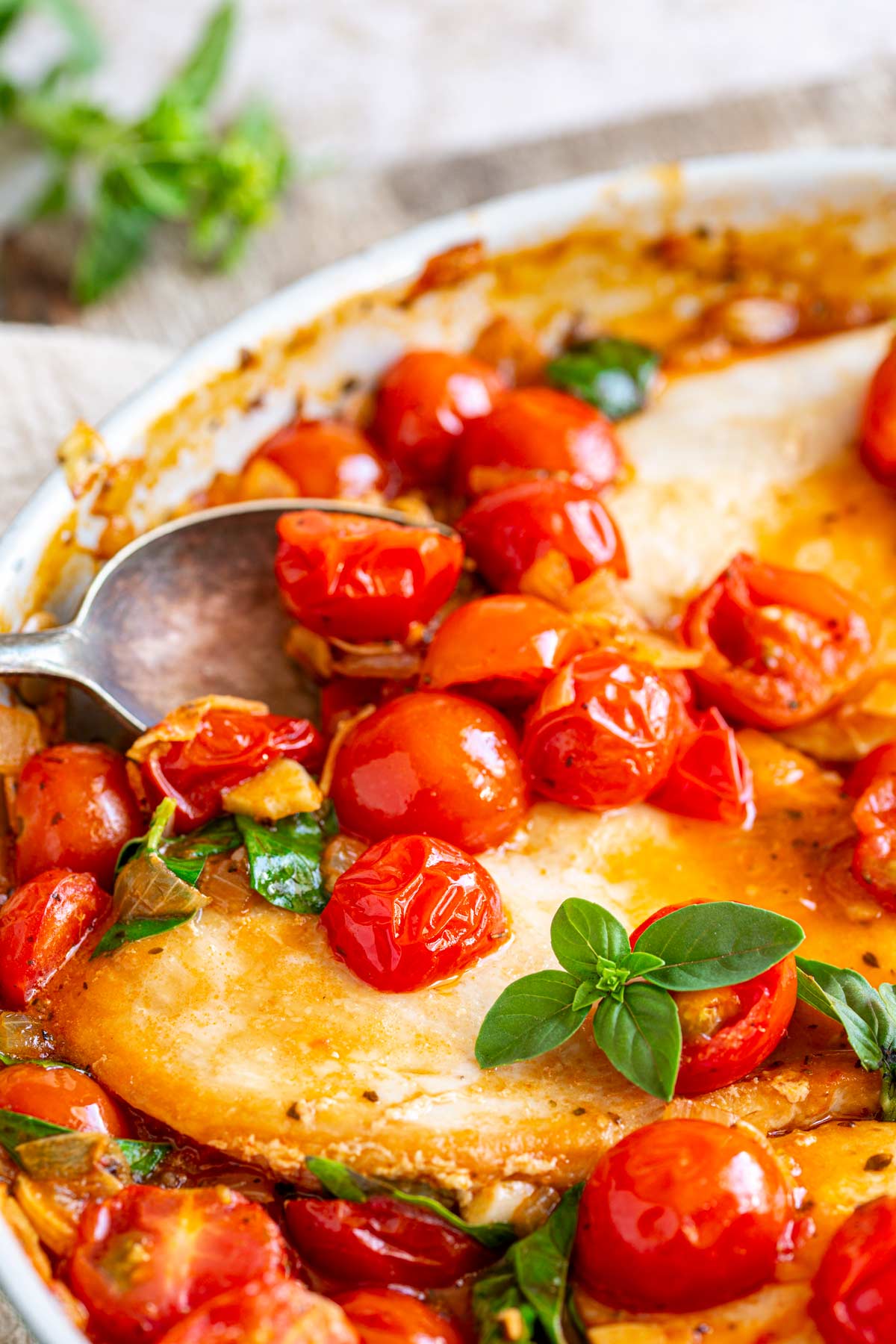 a spoon scooping up cooked cherry tomatoes from a skillet