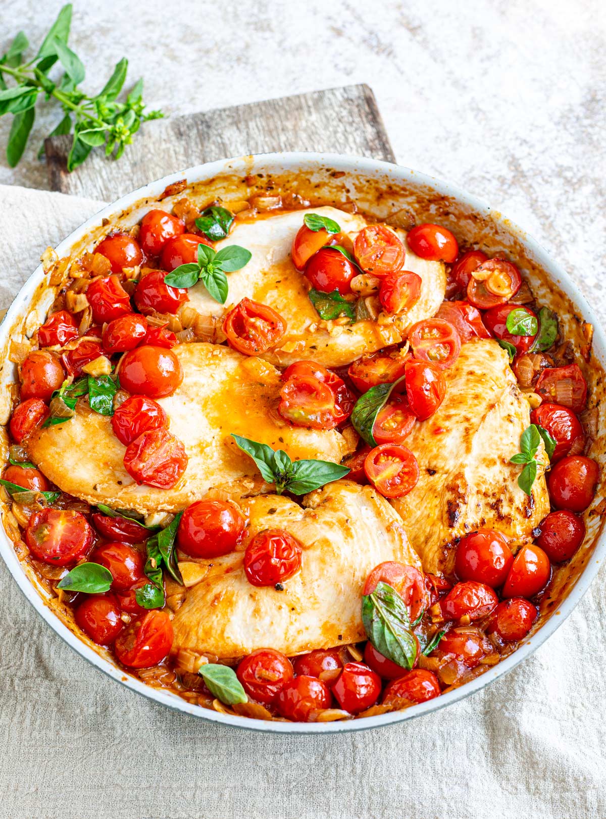 overhead of a skillet of chicken pomodoro on a rustic table with basil