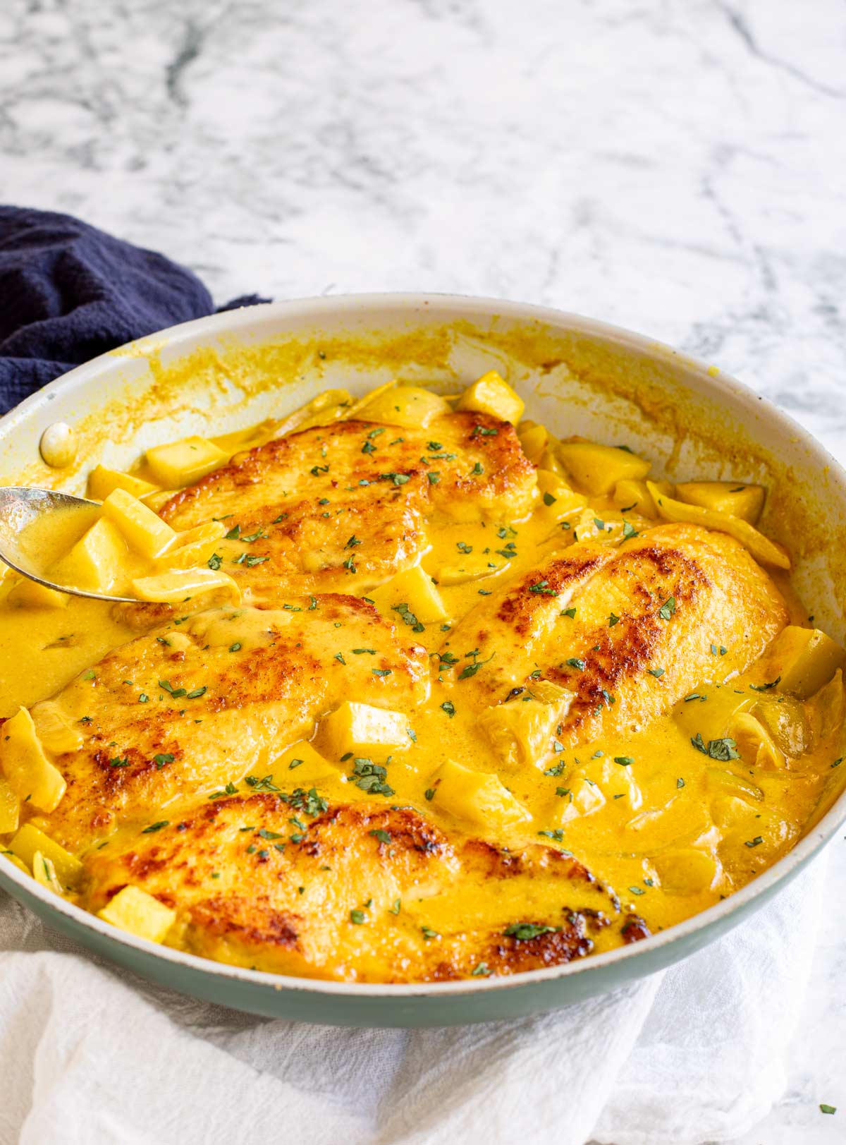 a spoon in a pan of creamy curried chicken breasts on a marble table