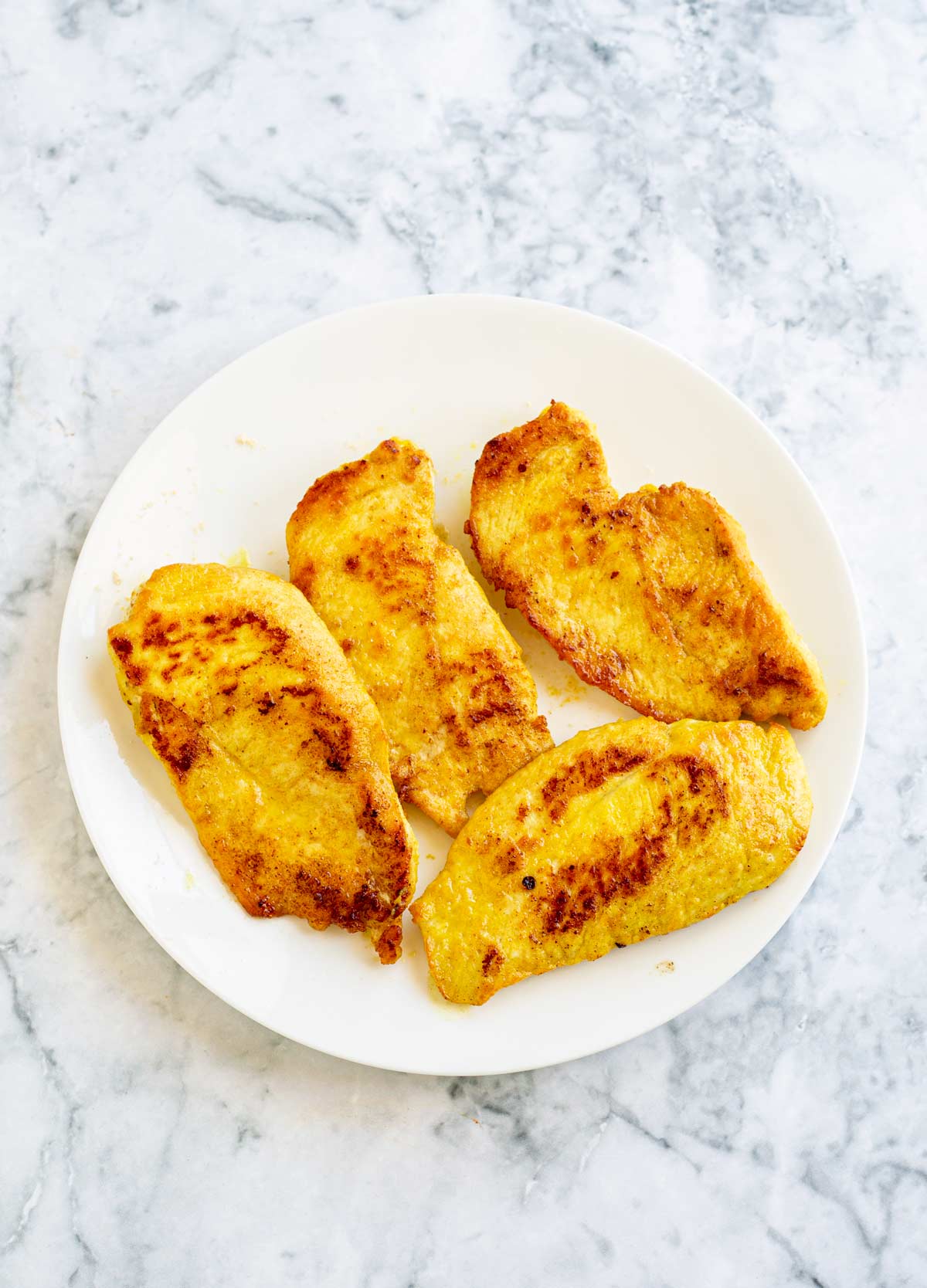 four cooked curry chicken breasts on a white plate