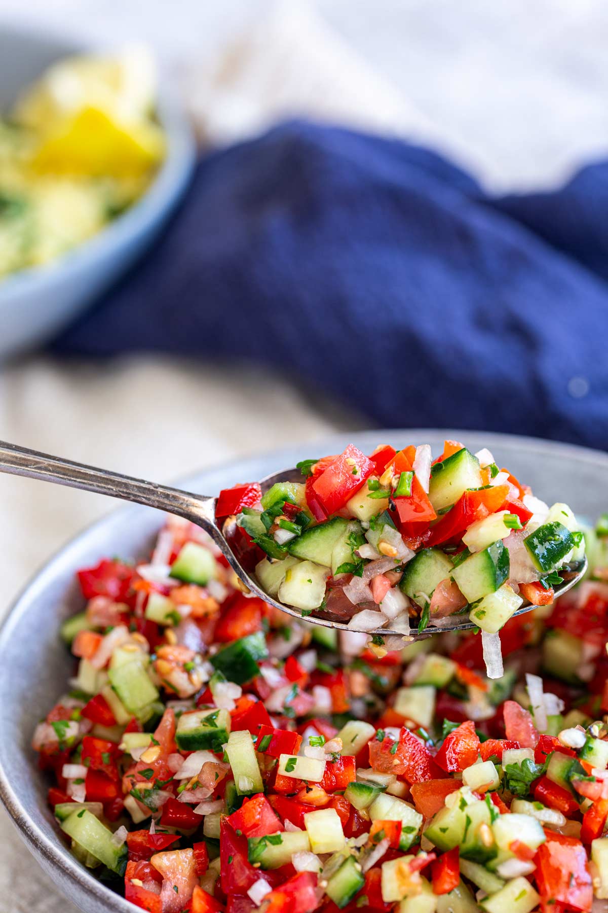 a spoon scooping a tomato salad out of a grey bowl