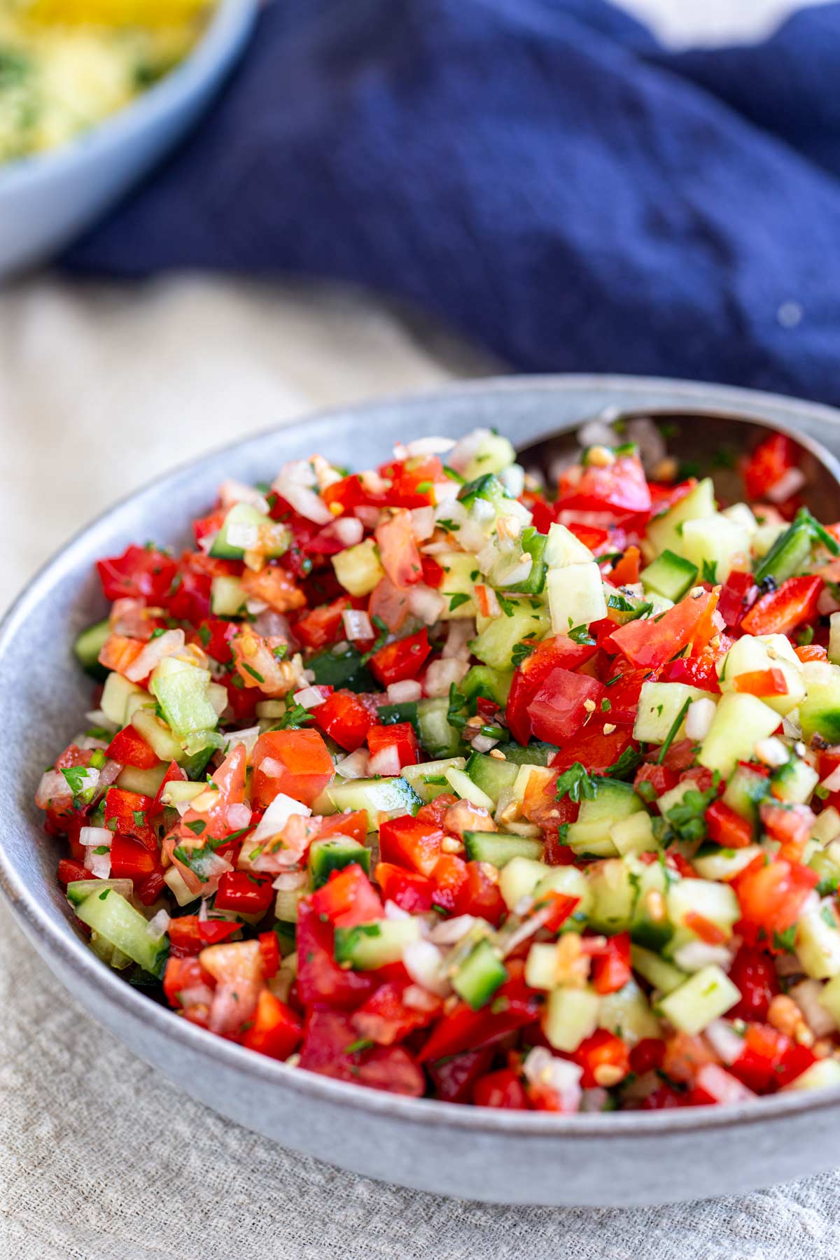 a grey bowl filled with a salad of finely chopped tomato, cucumber and onion and herbs