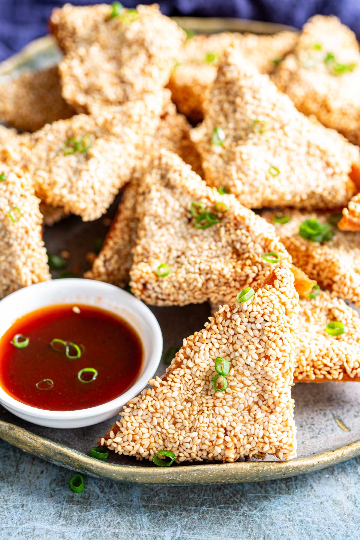 a plate of fired sesame coated triangles on a rustic blue plate