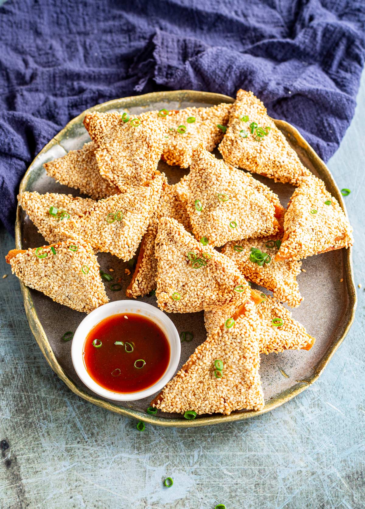 a grey plate with triangles of sesame toast on it with a blue napkin behind