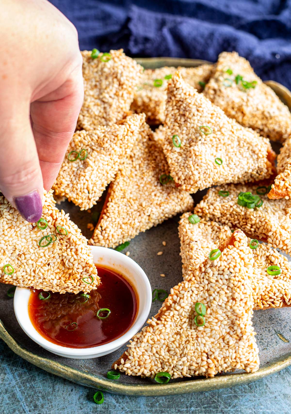 a hand dipping a triangle of chicken toast into chili sauce