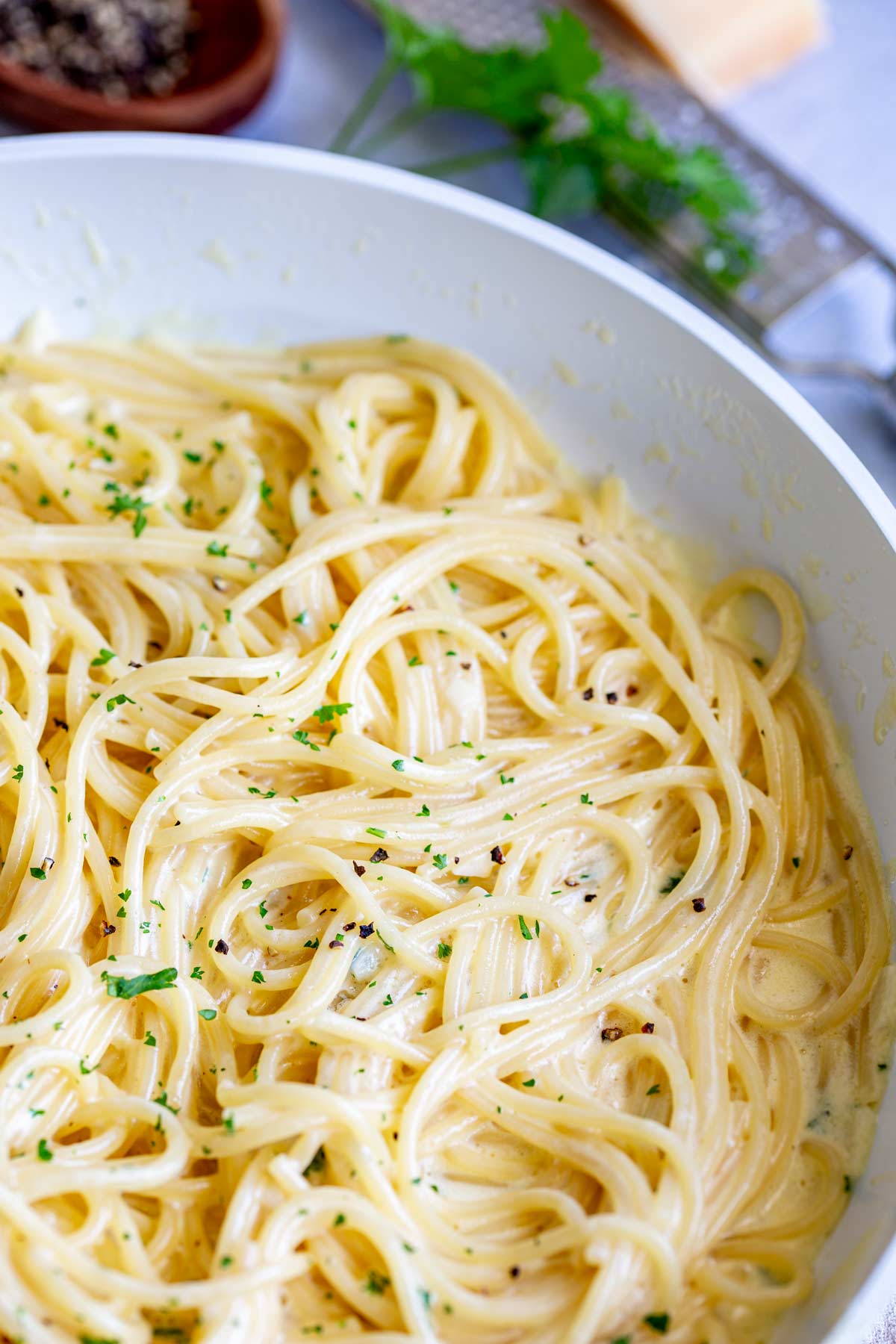 a skillet full of creamy spaghetti with parsley and pepper garnish