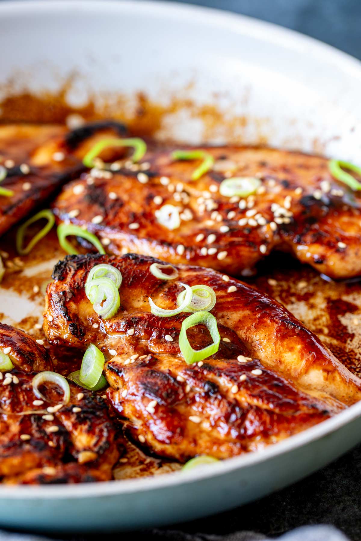 Rich, glossy glazed chicken breasts in a skillet, topped with sesame seeds and sliced green onions, .