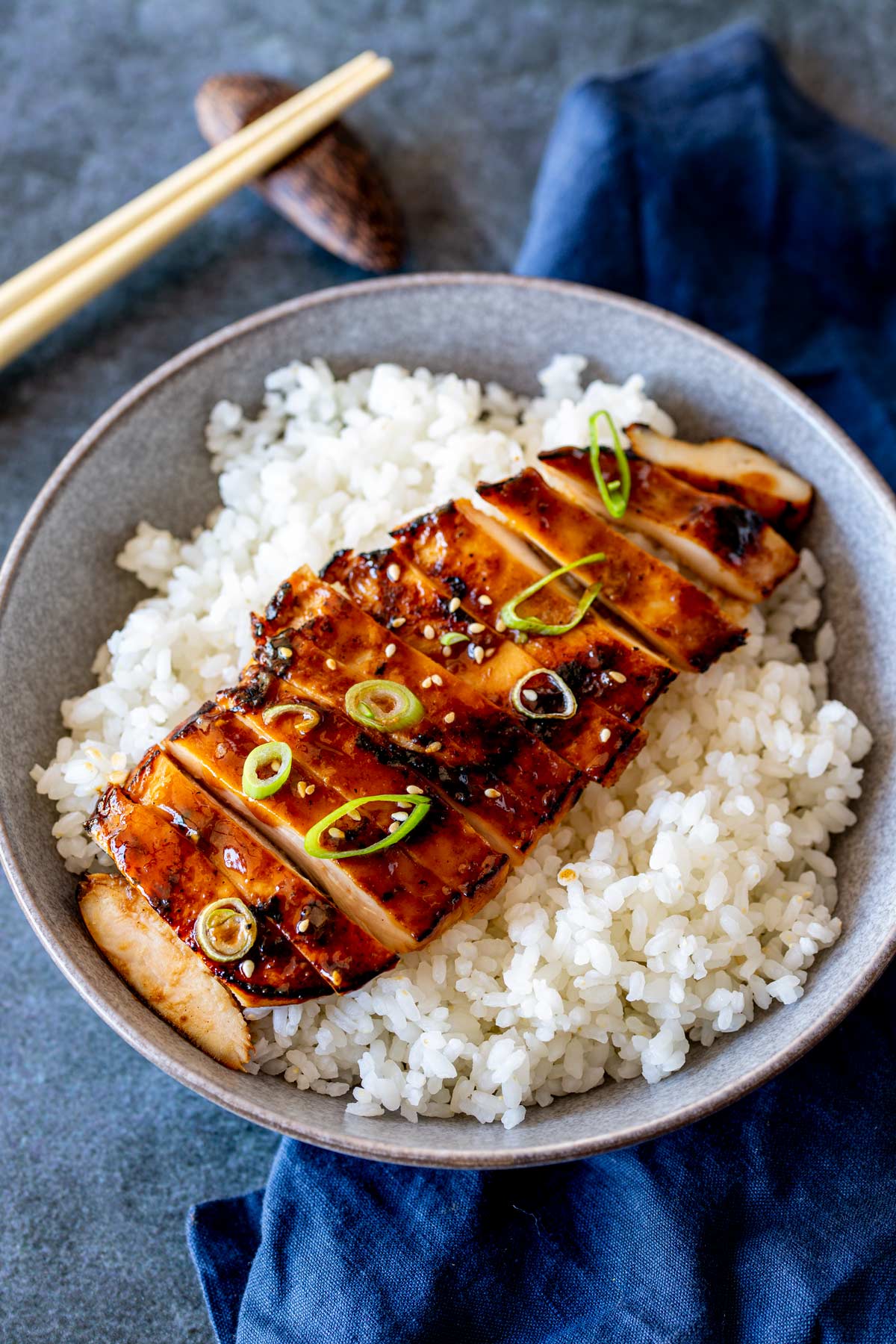 Thinly sliced miso chicken served on white rice with chopsticks resting beside the bowl.