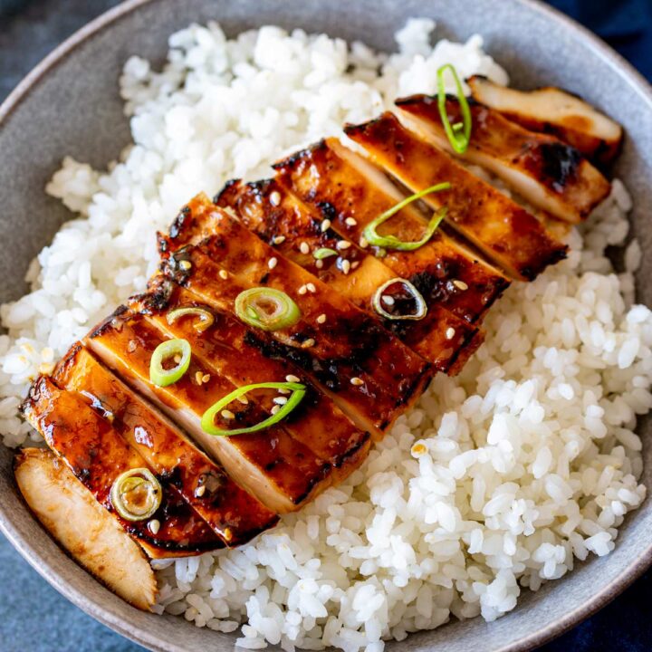 A close-up shot capturing the juicy and perfectly glazed piece of grilled chicken on top of white rice