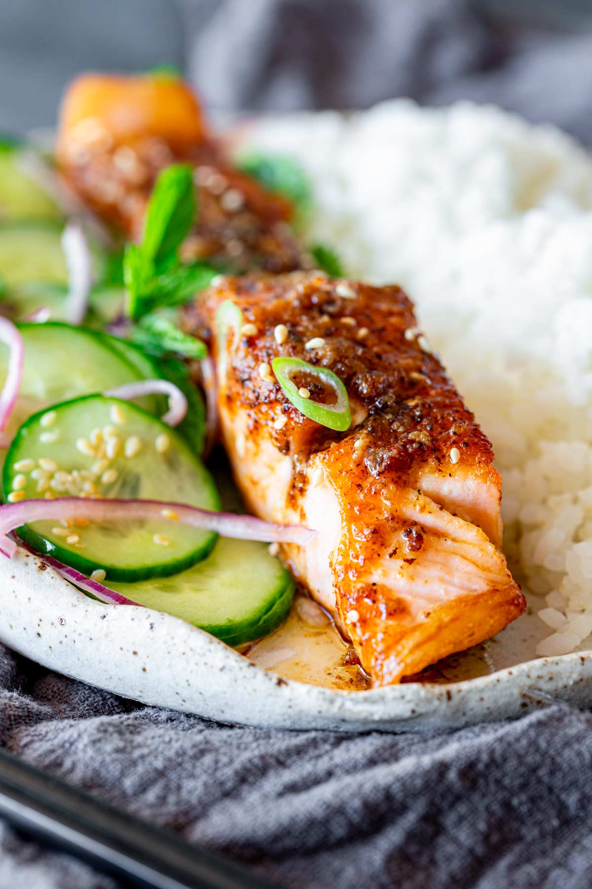 close up on a fillet of miso butter salmon fillet alongside white rice and a cucumber red onion salad