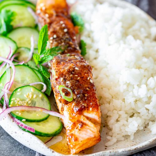 close up of a salmon fillet covered in miso butter with rice and salad next to it