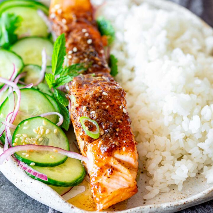 close up of a salmon fillet covered in miso butter with rice and salad next to it