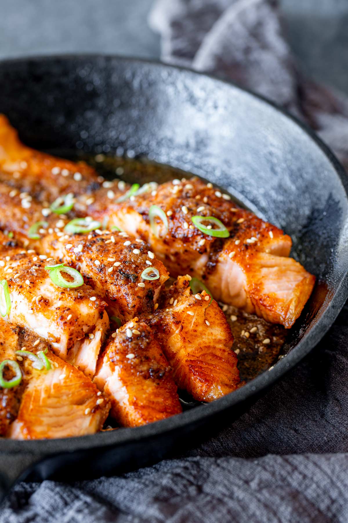Close-up of seared salmon fillets in a black cast iron skillet, topped with sesame seeds and sliced green onions