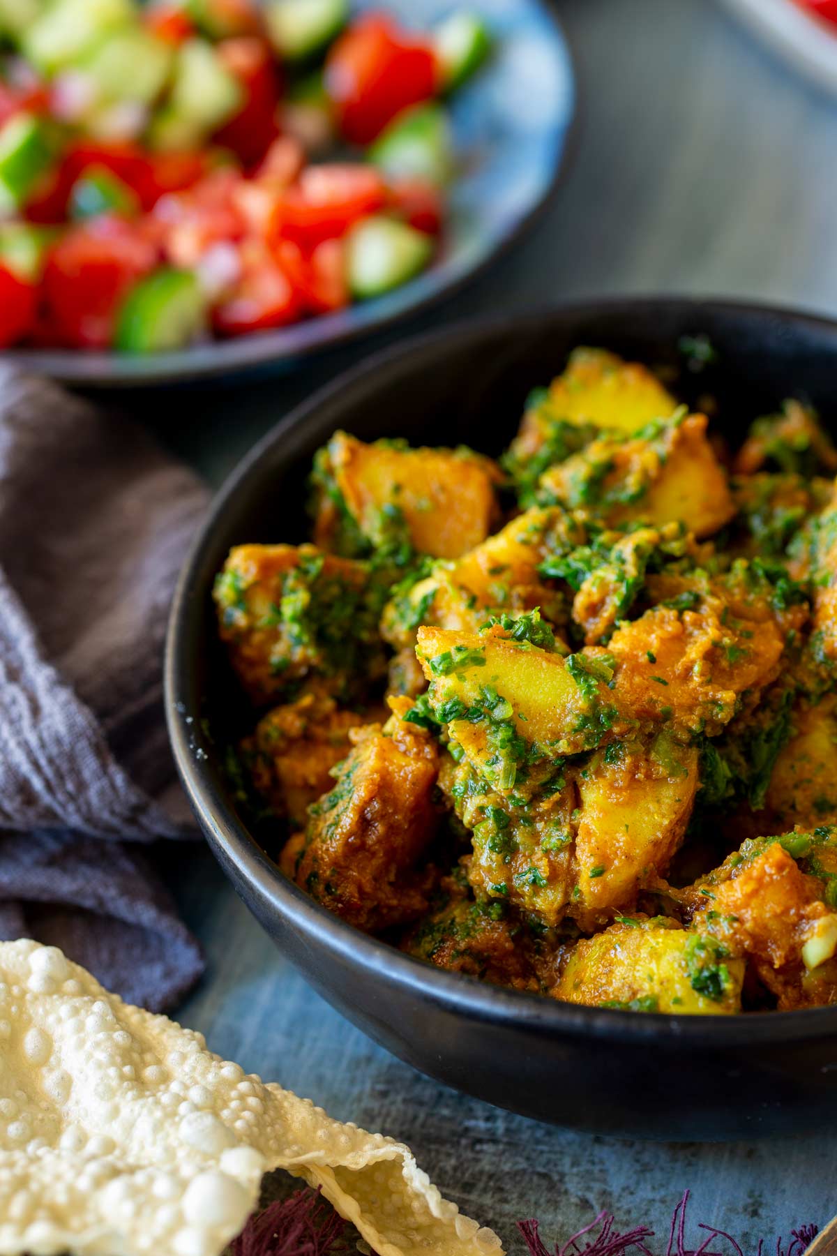A black bowl of saag aloo, highlighting the golden potato chunks coated in a vibrant spinach and curry sauce