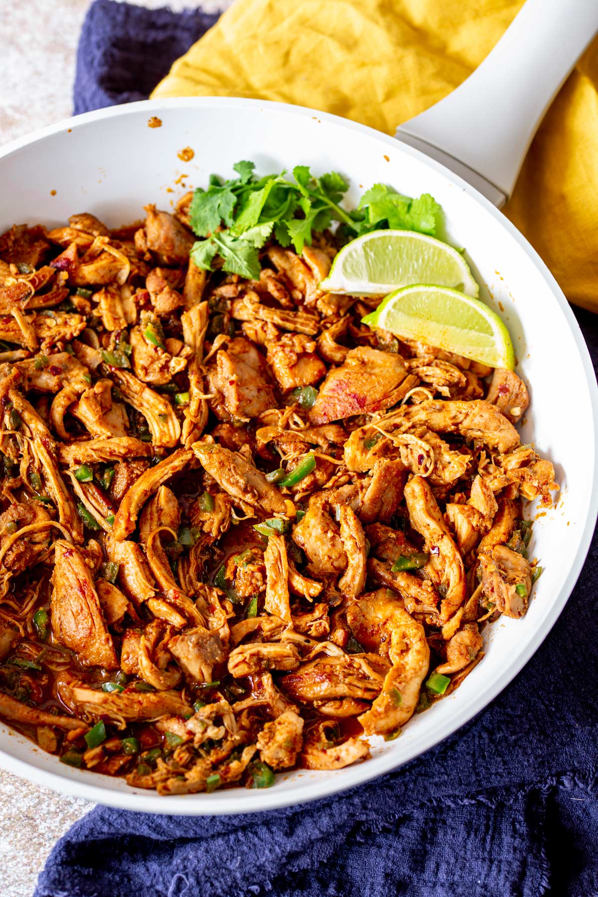 a skillet of taco chicken on a table with blue and yellow napkins