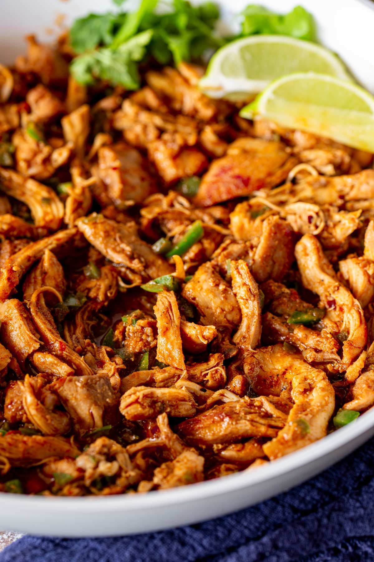 shredded chicken in a taco sauce in a white skillet with wedges of lime