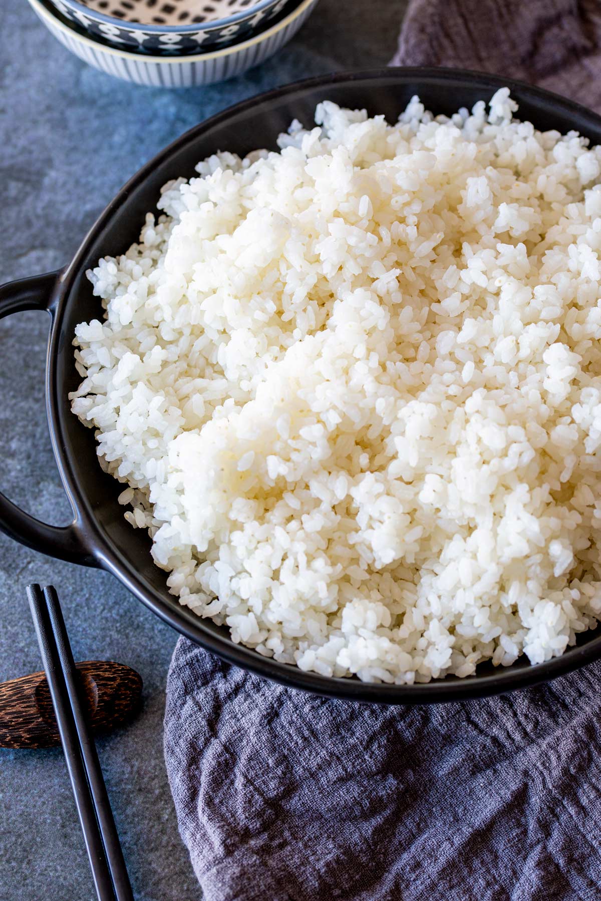overhead of a black bowl filled with white rice on a blue table