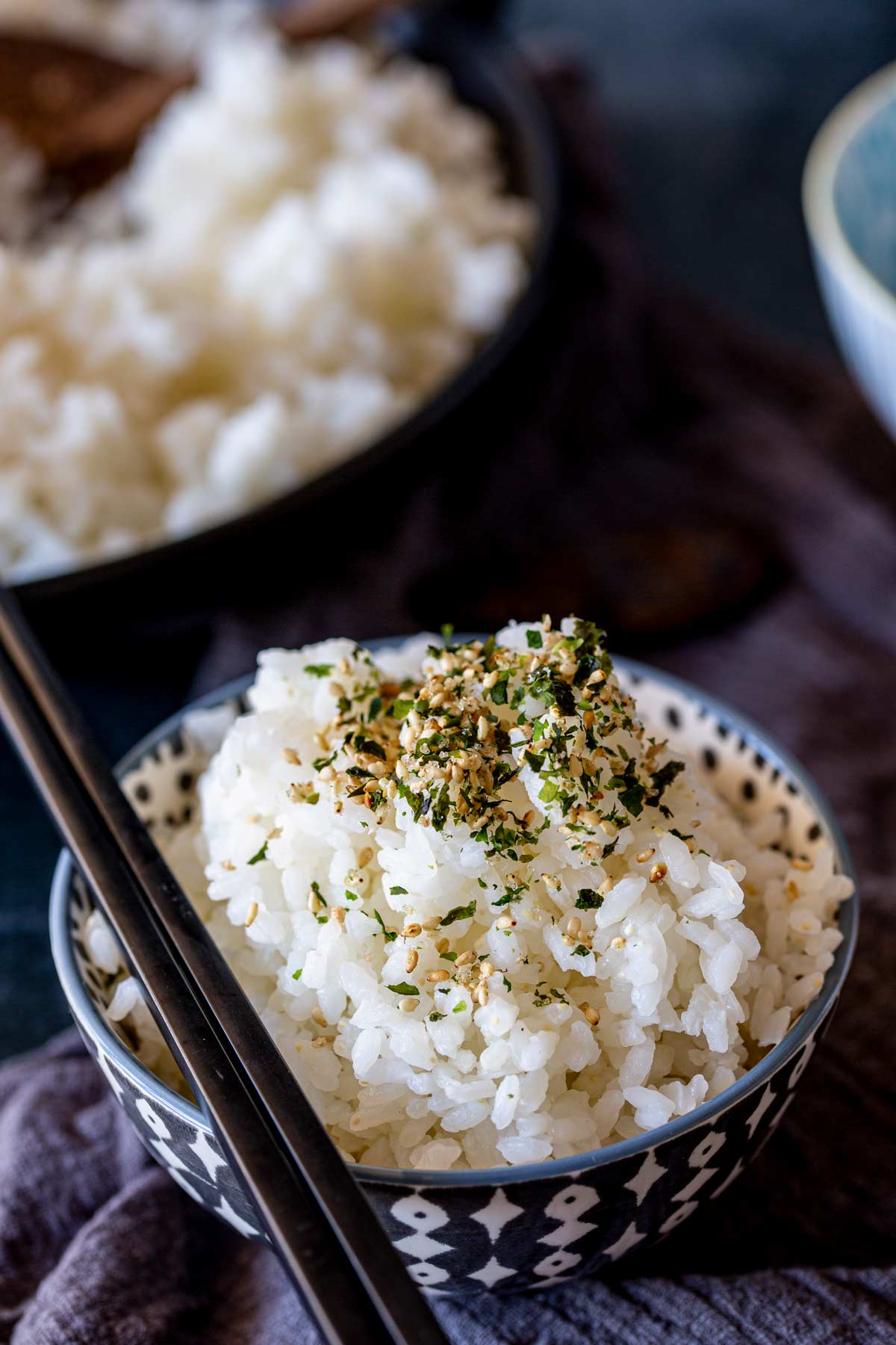 chopsticks set on the top of a bowl of rice with sesame seasoning on it