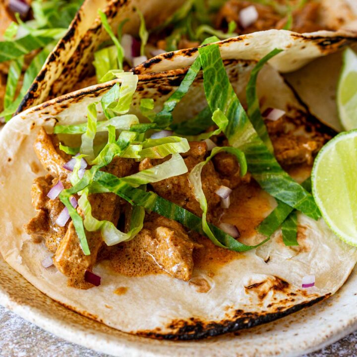 Closeup of a soft flour tacos stuffed with creamy chicken, garnished with lettuce and finely chopped red onion on a speckled plate.