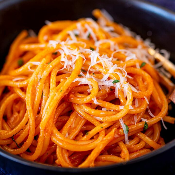 close up on a black bowl filled with orange sauced pasta, garnished with shredded Parmesan cheese and herbs, with a fork beside for serving