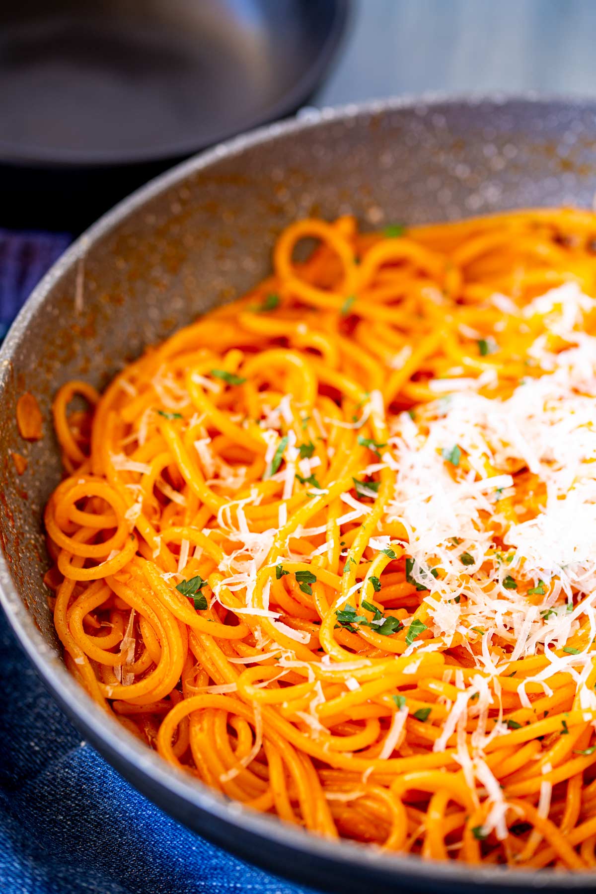 A skillet full of spaghetti noodles coated in a gochujang butter sauce, topped with a generous amount of finely grated cheese and green herb sprinkled over