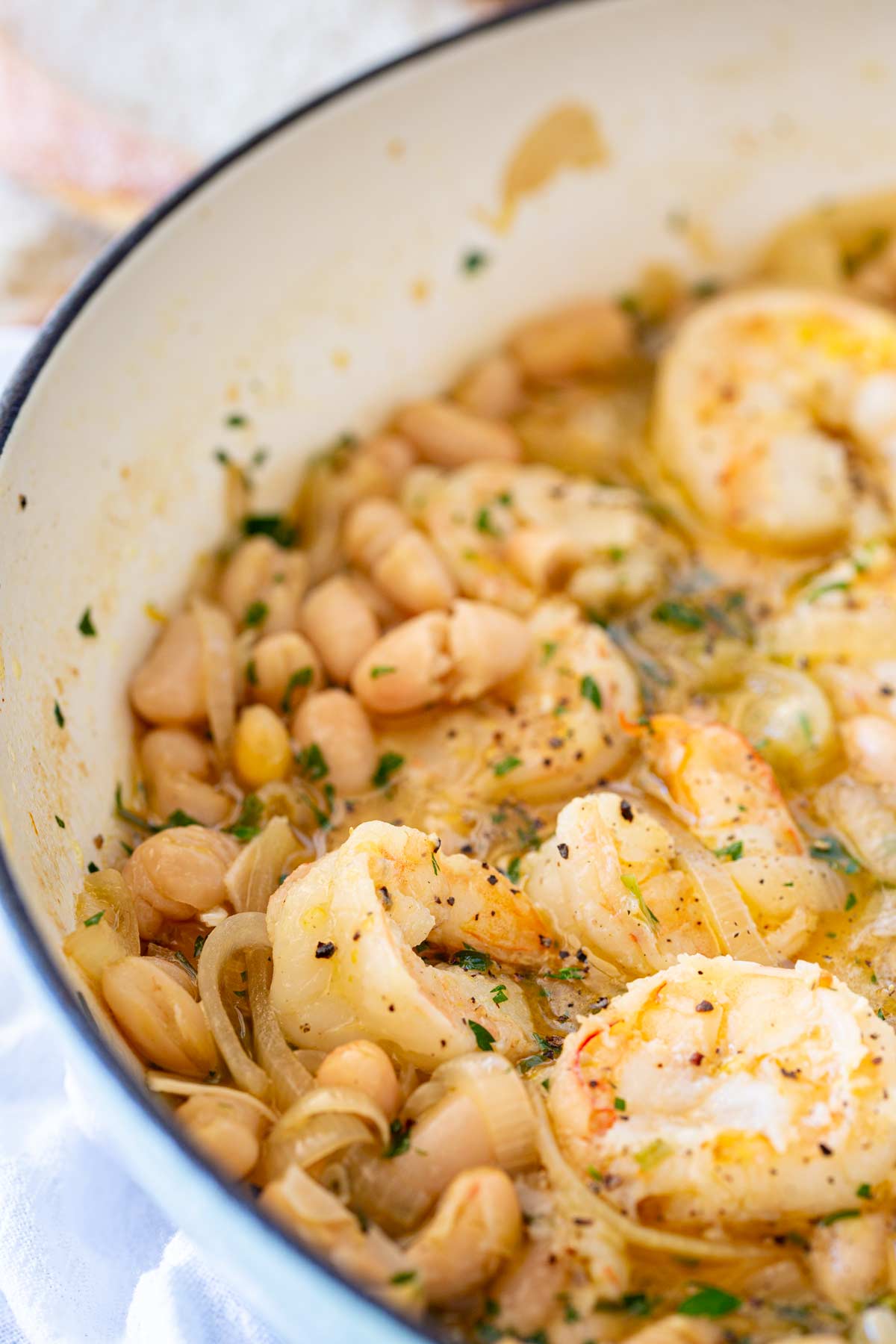 Ccooked shrimp nestled among tender beans, sliced onions, and a seasoned broth.