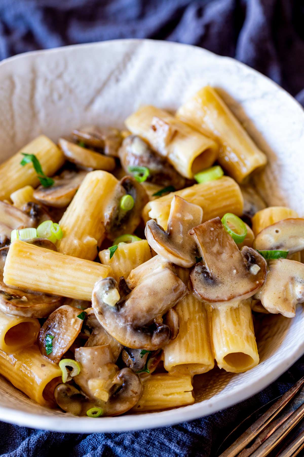 A serving of rigatoni pasta in a creamy miso sauce, topped with sautéed mushrooms and green onions, served in a white bowl.