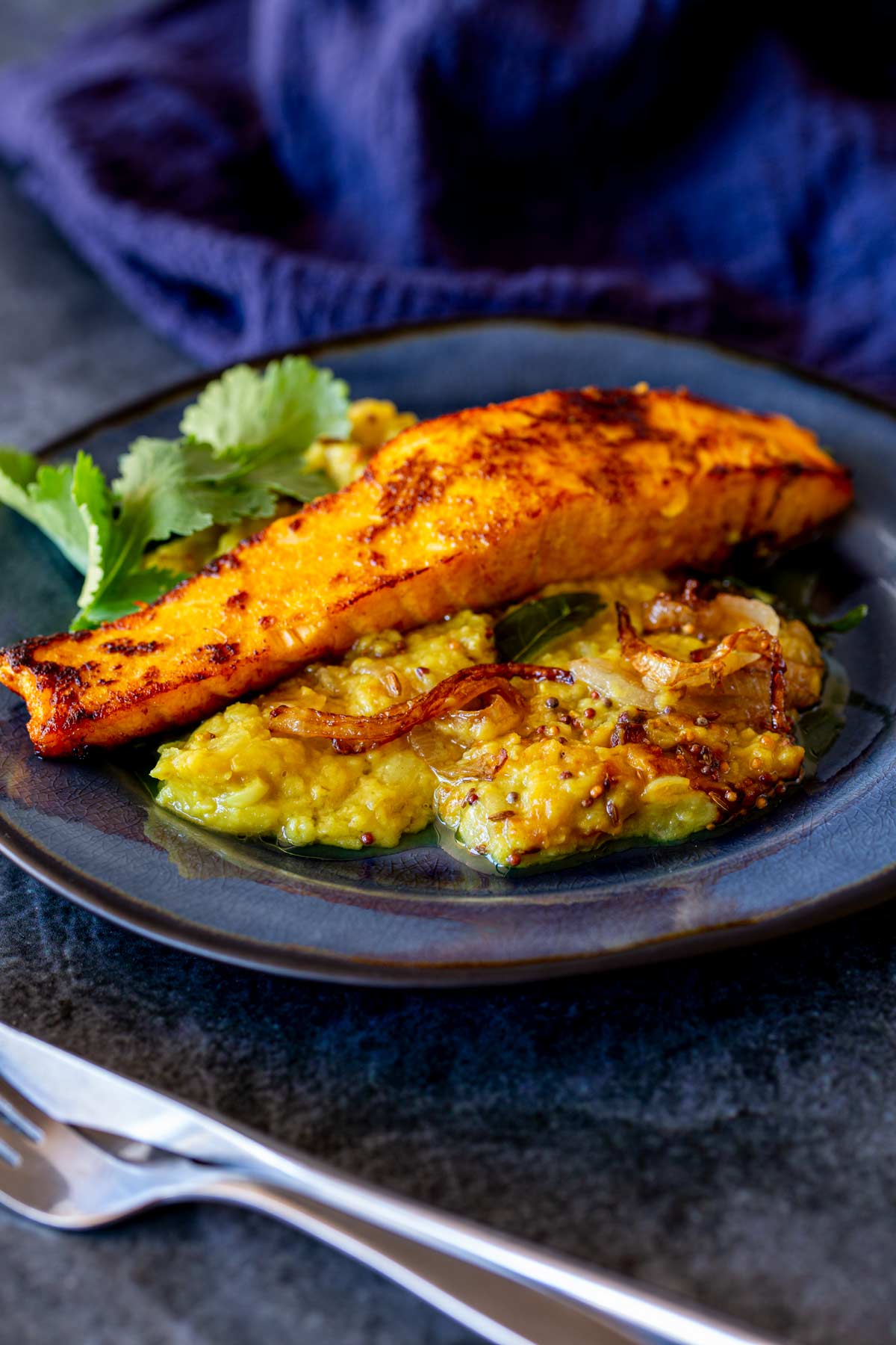 a blue plate with a Seared salmon fillet served with lentil daal and some fresh cilantro