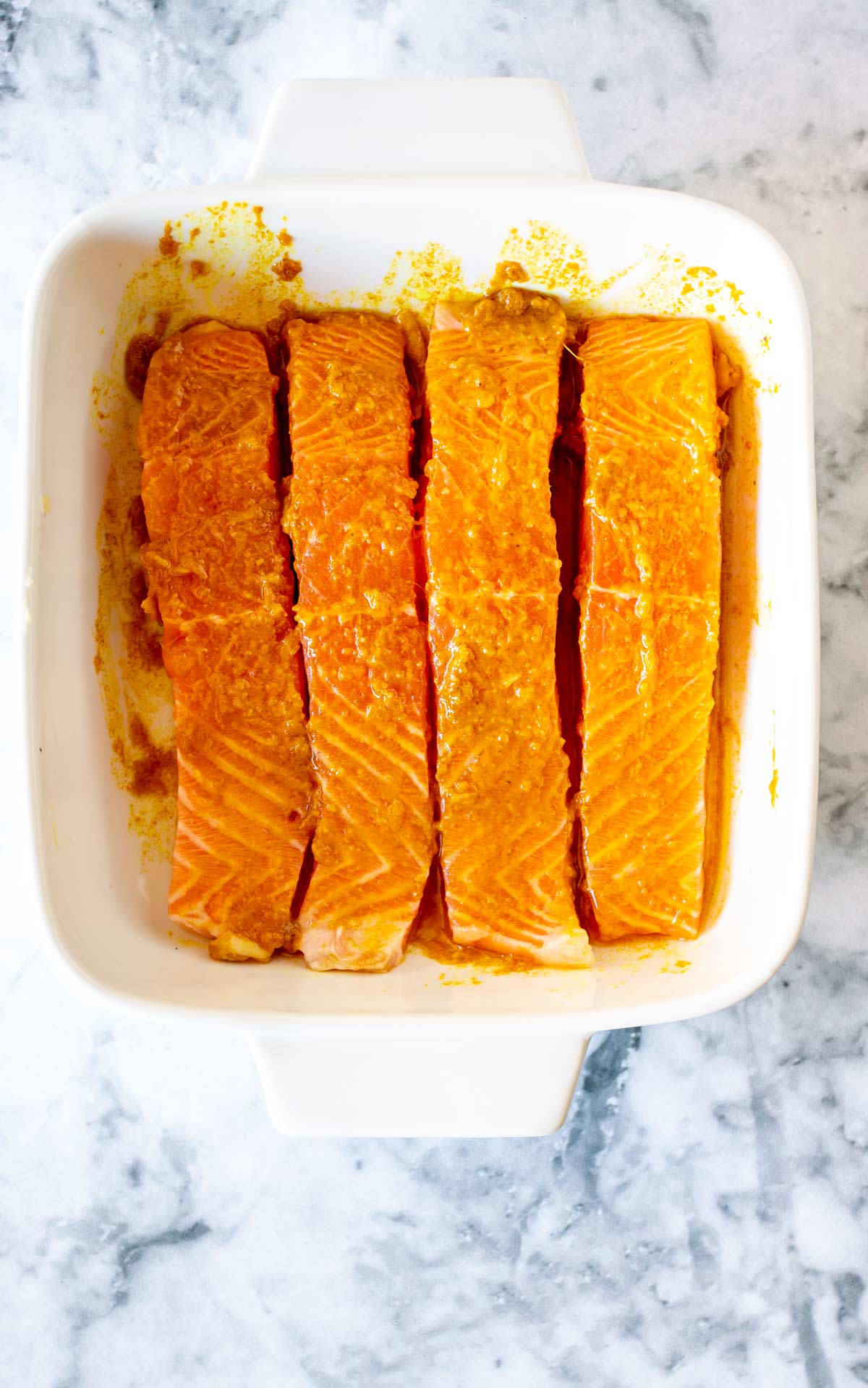 a white dish with raw marinated salmon in it on a marble bench top