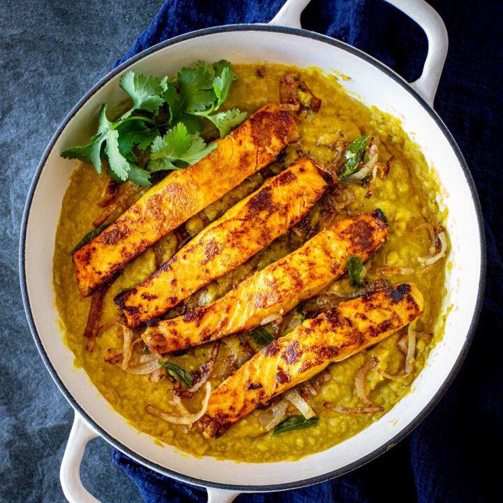 Seared salmon on top of golden lentil daal in a white skillet on a blue table