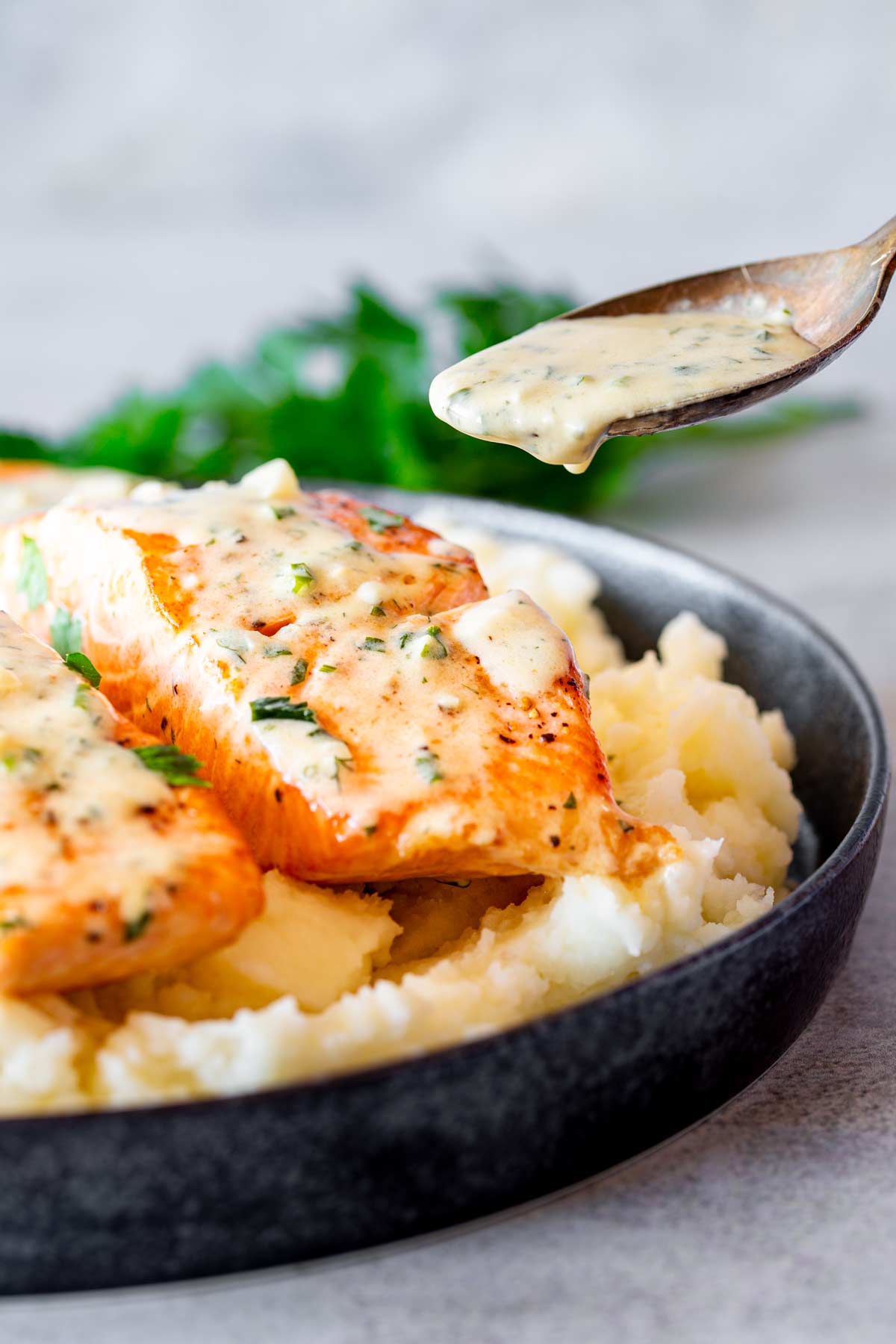 a spoon drizzling a creamy sauce over a salmon fillet on a bed of mashed potato