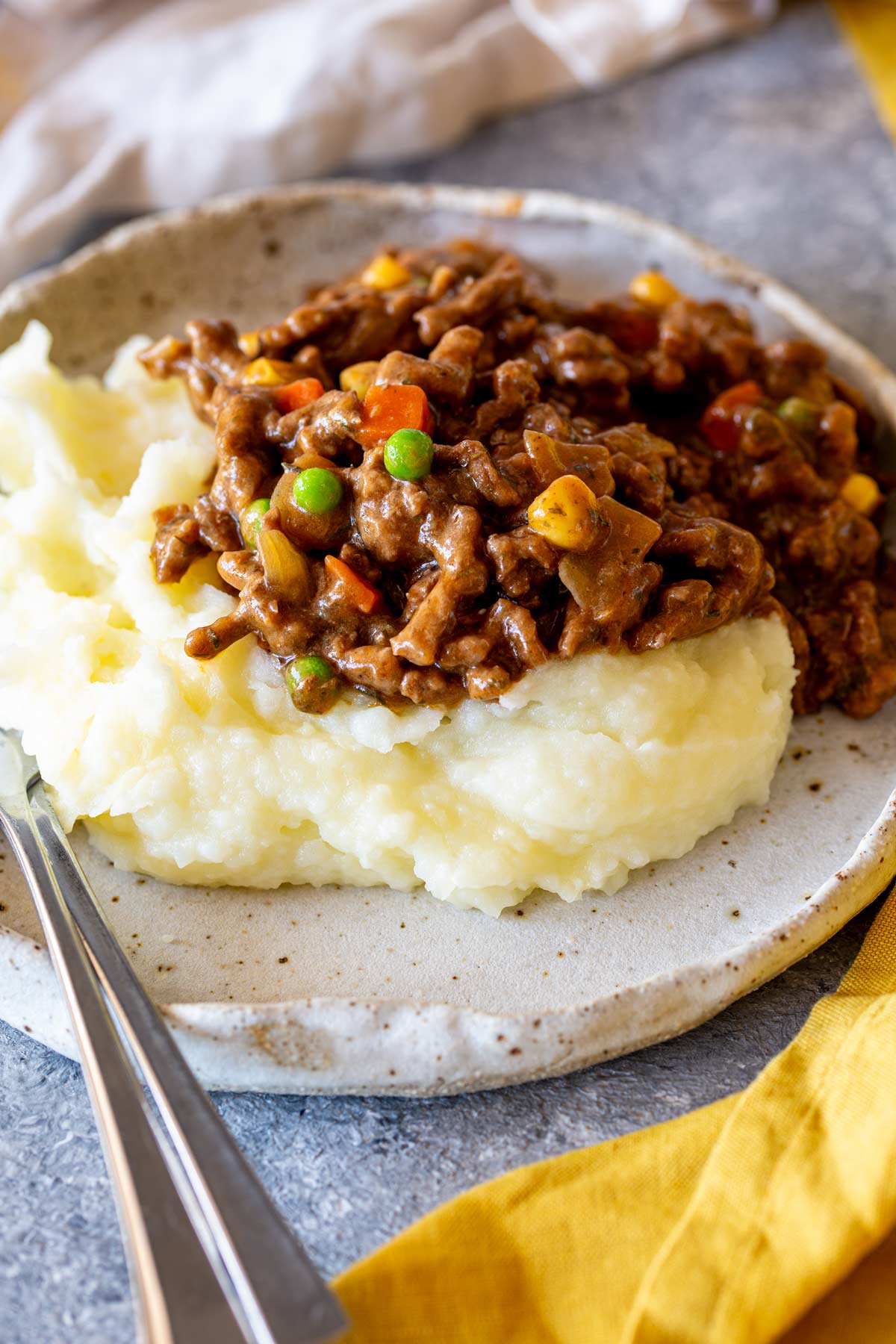 A plate of ground beef casserole served on a bed of mashed potatoes, with a yellow napkin