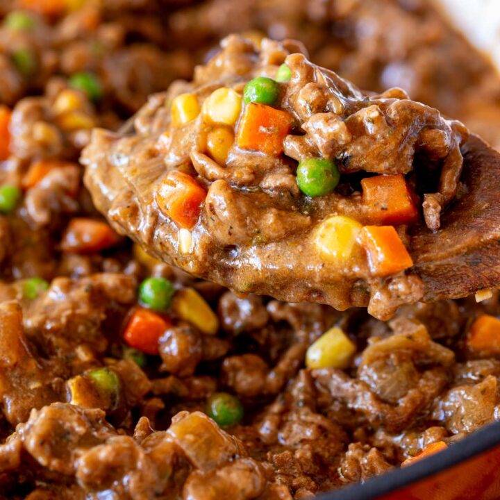 extreme close up of a wooden spoon scooping up saucy ground beef and vegetables from a pan
