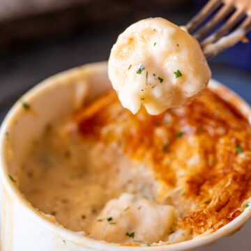 A forkful of creamy seafood filling with hints of parsley lifted from a ramekin, showcasing the flaky top layer of a freshly baked pot pie