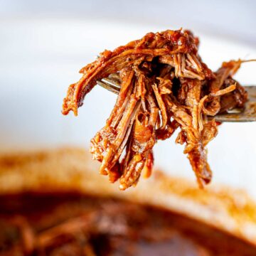 A close-up of tender shredded BBQ beef, glistening in a rich, smoky sauce, lifted by a