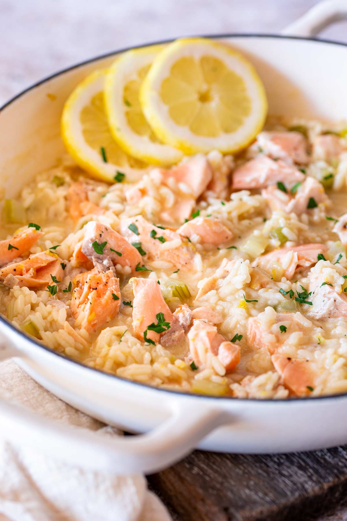 A creamy Sicilian-style risotto topped with chunks of cooked salmon and garnished with fresh lemon slices, in a white pot.