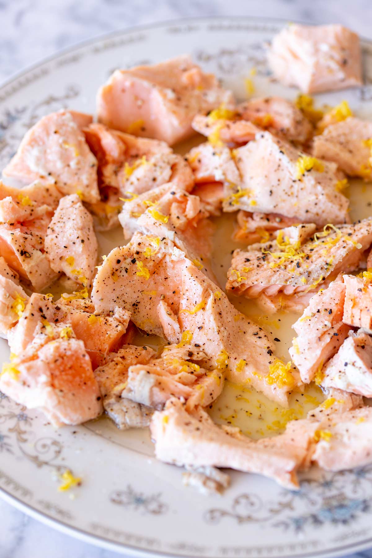 A plate of bite-sized salmon pieces, lightly peppered, with bright yellow lemon zest scattered on top, capturing the texture and freshness of the salmon and zest.
