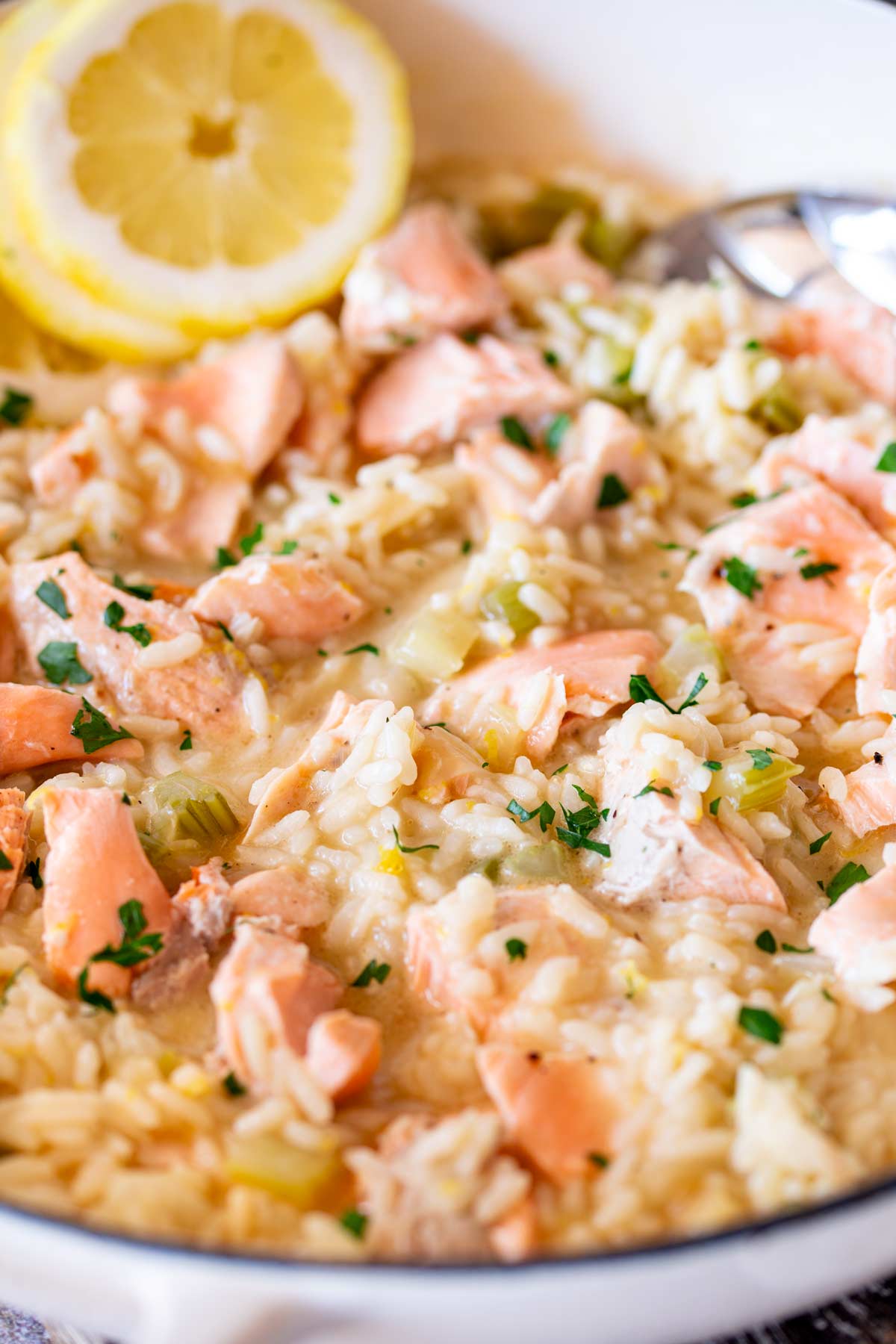 A creamy Sicilian-style risotto topped with chunks of cooked salmon and garnished with fresh lemon slices, in a white pot.