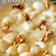 Pin Image: Gnocchi in a gorgonzola sauce with walnuts in a white skillet, with a rosemary sprig on the side. with text overlaid
