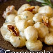 Pin Image: Gnocchi in gorgonzola sauce with walnuts on a brown plate and a rosemary sprig with text overlaid