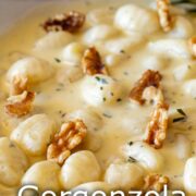 Pin Image: Gnocchi in a gorgonzola sauce with walnuts in a white skillet, with a rosemary sprig on the side. with text overlaid