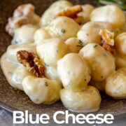 Pin Image: Gnocchi in gorgonzola sauce with walnuts on a brown plate and a rosemary sprig with text overlaid